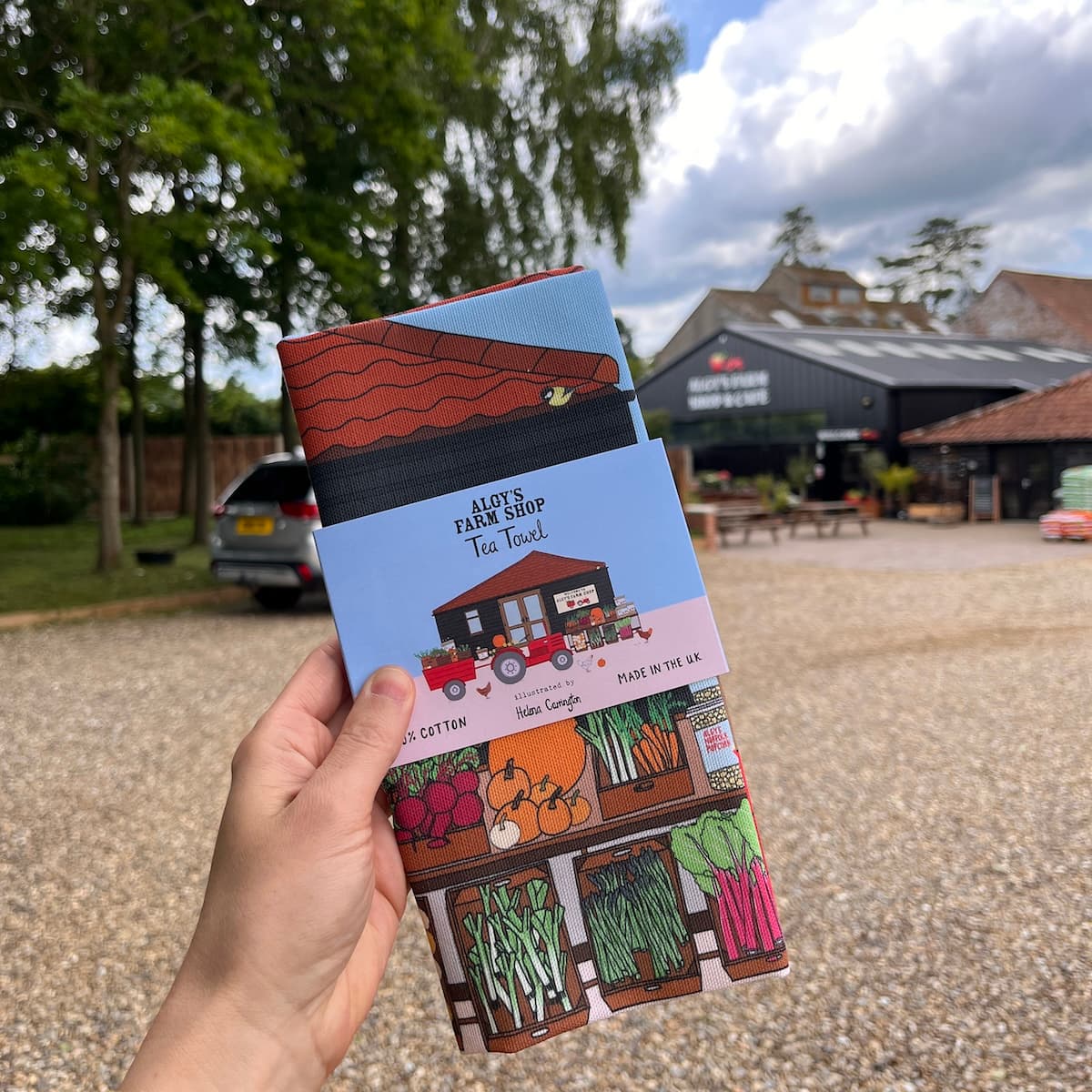 Photo of Algys Farm Shop tea towel held in front of the Algys Farm Shop building
